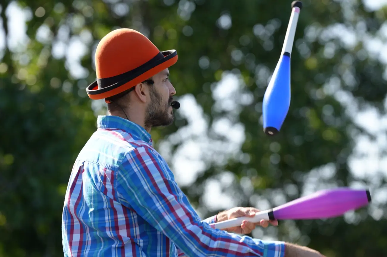 A juggler in an orange bowler hat spinning blue and pink clubs